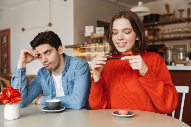 Hombre mirando exasperado junto a una mujer fotografiando comida